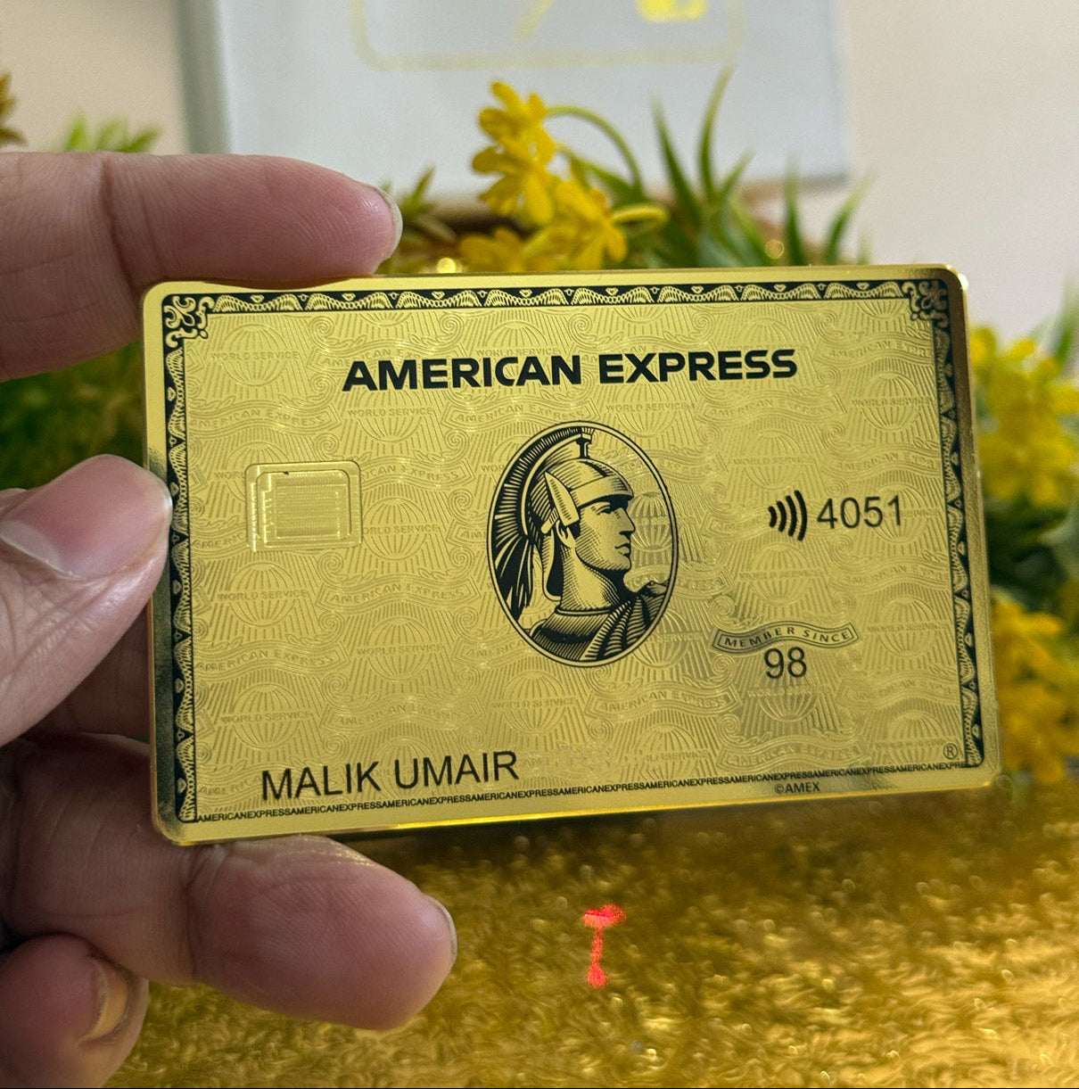 24k Gold American Express card held by a hand with a blurred background